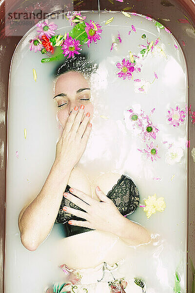 Frau im BH nimmt ein Milchbad mit Blüten