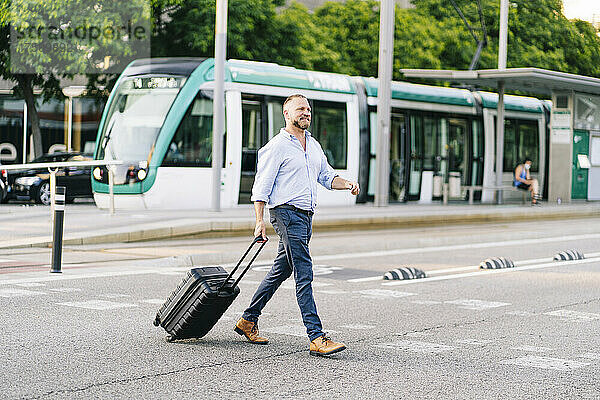 Geschäftsmann mit Rollgepäck überquert Straße in der Stadt