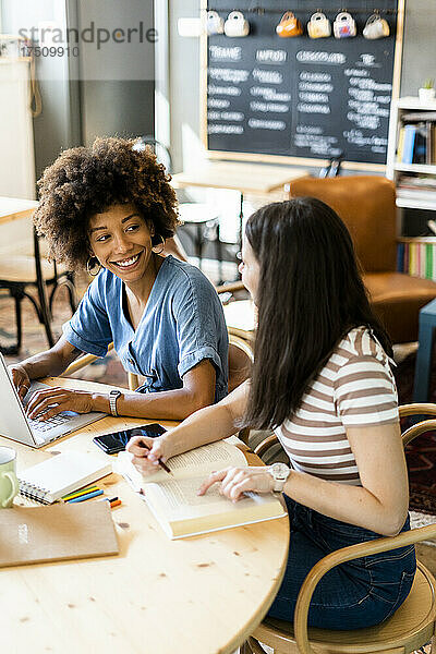 Glückliche Frauen lernen mit Laptop am Tisch im Café