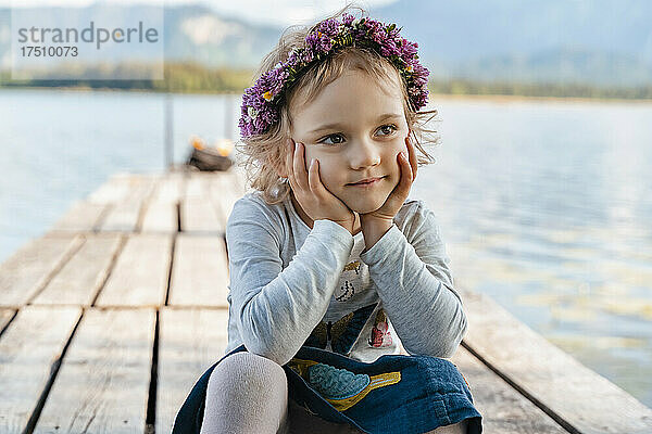 Nahaufnahme eines süßen Mädchens mit Tiara  das auf einem Steg am See sitzt