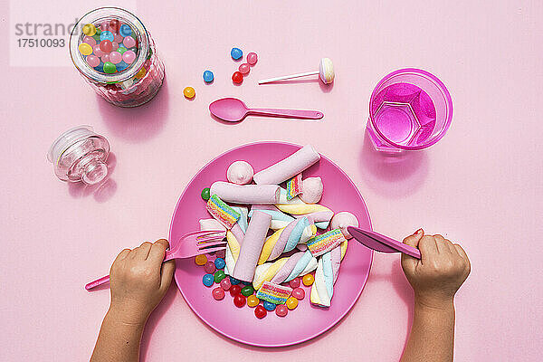 Hände eines kleinen Mädchens  das sich darauf vorbereitet  einen mit verschiedenen Süßigkeiten gefüllten Teller zu essen