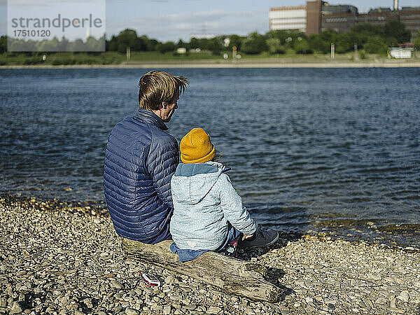 Vater und Tochter blicken an einem sonnigen Tag auf einen Baumstamm und blicken auf den Rhein