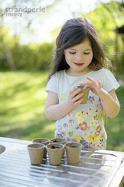 Nettes Mädchen pflanzt Samen in kleine Töpfe auf dem Tisch im Garten
