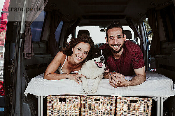 Lächelndes Paar mit Hund im Wohnwagen liegend