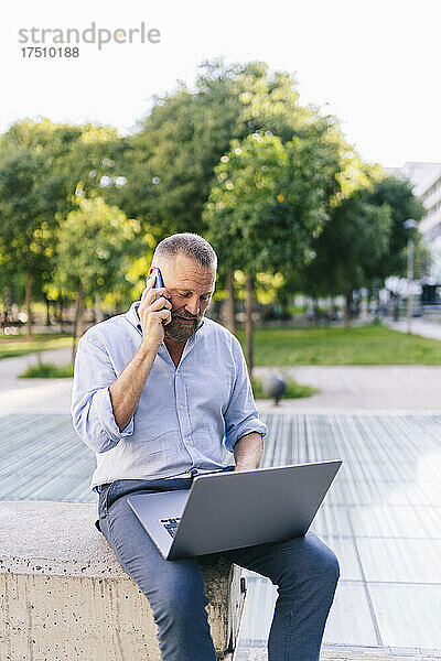 Geschäftsmann spricht auf Smartphone  während er Laptop im Büropark benutzt