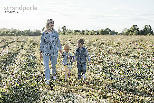 Lächelnde Mutter mit zwei Kindern  die auf dem Feld spazieren