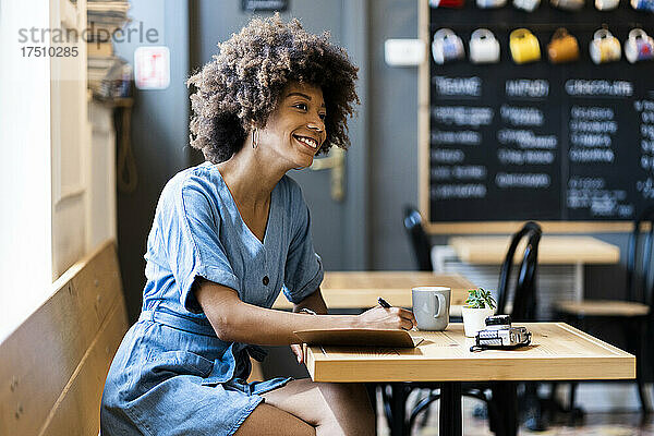 Nachdenkliche Frau schreibt in ein Buch  während sie am Tisch im Café sitzt