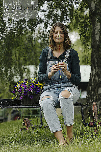 Junge Frau sitzt neben einem Blumenkasten und hält einen Grashalm