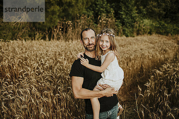 Lächelnder Vater trägt Tochter im Weizenfeld