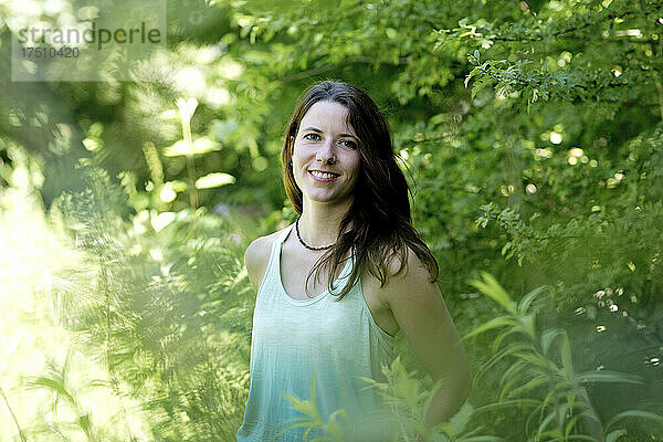 Lächelnde junge Frau  die inmitten von Pflanzen im Wald steht