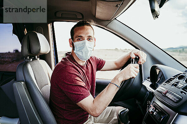 Mann mit Gesichtsmaske sitzt während COVID-19 im Auto