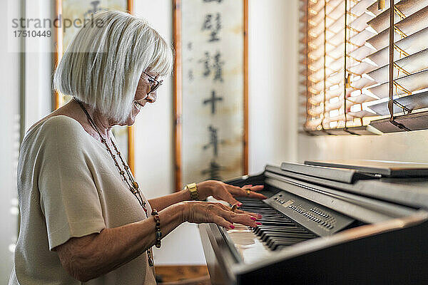 Lächelnde ältere Frau mit Sonnenbrille  die zu Hause Klavier spielt