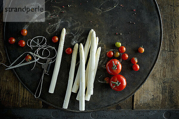 Tomatoes and peeled asparagus stalks on rustic baking sheet