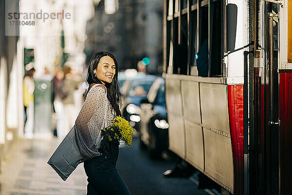 Lächelnde junge Frau steht neben der Straßenbahn auf der Straße