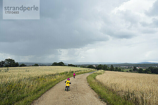 Mädchen mit Fahrrad und Laufrad auf Feldweg  Regenwolken