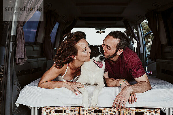 Lächelndes Paar küsst Hund  während es im Wohnwagen liegt