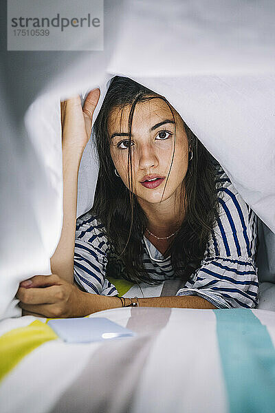 Schöne junge Frau liegt unter einer Decke auf dem Bett