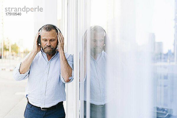 Geschäftsmann hört Musik über Kopfhörer  während er am Gebäude vorbeigeht