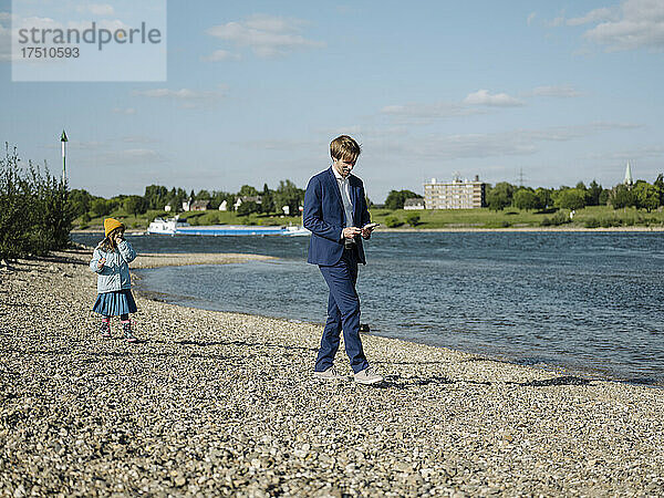 Geschäftsmann benutzt Smartphone  während er mit Tochter am Flussufer spaziert