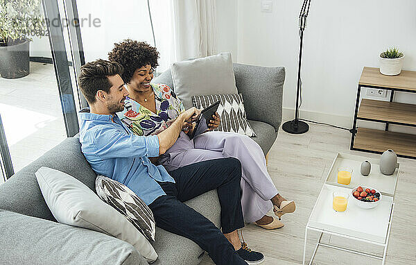 Glückliches Paar nutzt digitales Tablet  während es auf dem Sofa im Penthouse sitzt