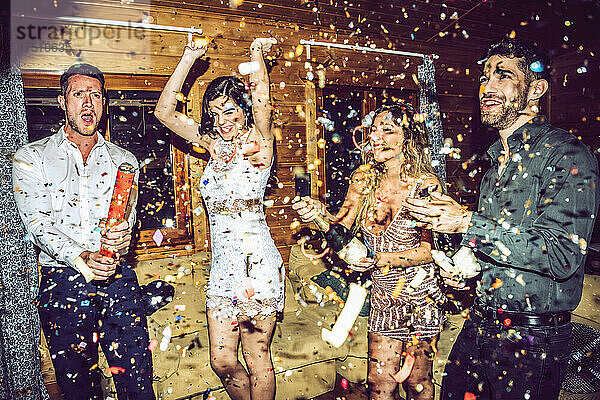 Fröhliche Freunde öffnen Champagner  während sie auf einer Party inmitten von Konfetti tanzen