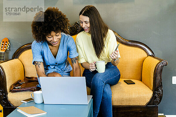 Fröhliche Frauen benutzen Laptop  während sie auf dem Sofa in einem modernen Café sitzen
