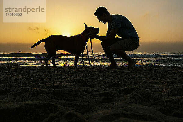Silhouette eines Mannes  der im Morgengrauen seine Freizeit mit Hund am Strand verbringt
