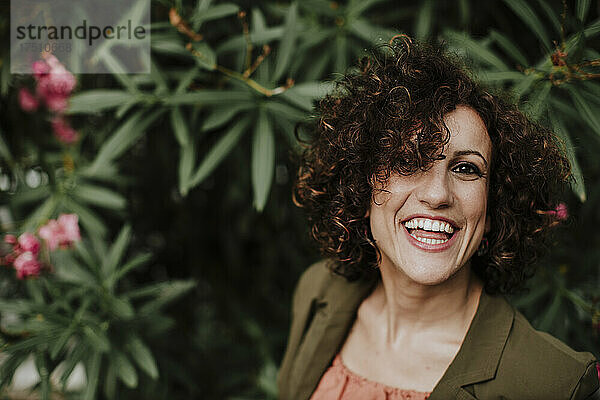 Nahaufnahme einer fröhlichen Frau mit lockigem Haar vor Pflanzen im Park