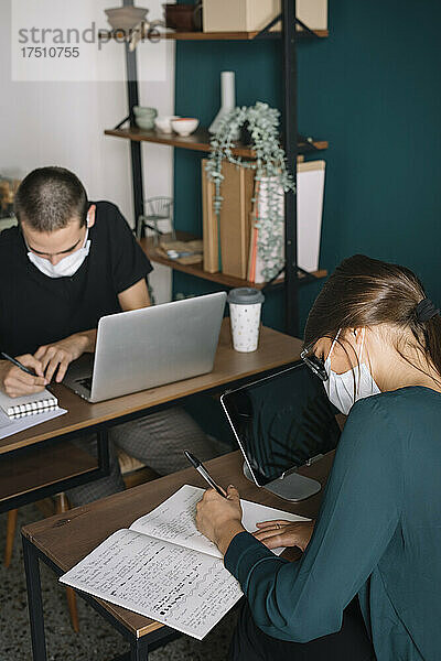 Junge Männer und Frauen tragen Schutzmasken und arbeiten zu Hause am Schreibtisch