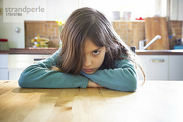 Verärgertes Mädchen sitzt in der Küche und lehnt sich an den Tisch