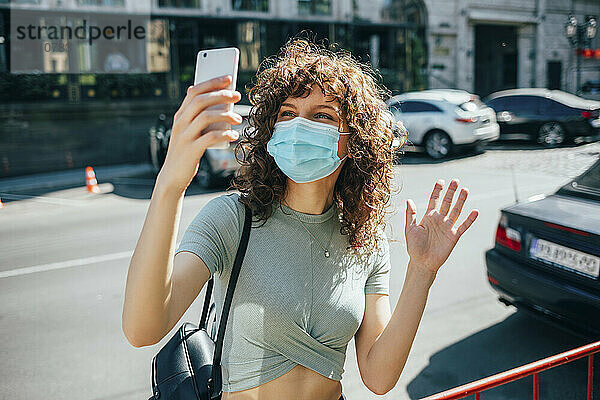 Frau trägt Schutzmaske und benutzt Smartphone in der Stadt