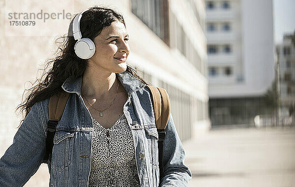 Junge Frau hört Musik über Kopfhörer und schaut weg  während sie in der Stadt steht