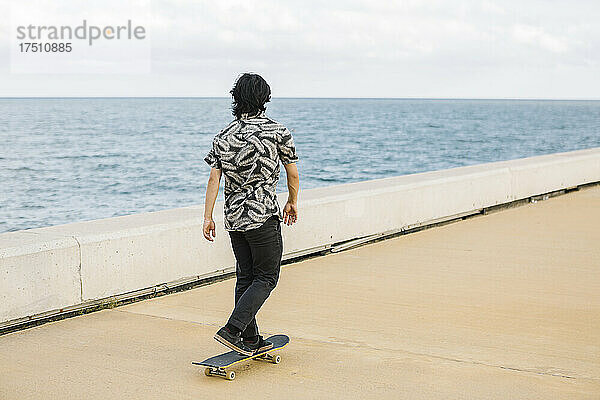 Junger Mann fährt Skateboard auf der Strandpromenade der Stadt
