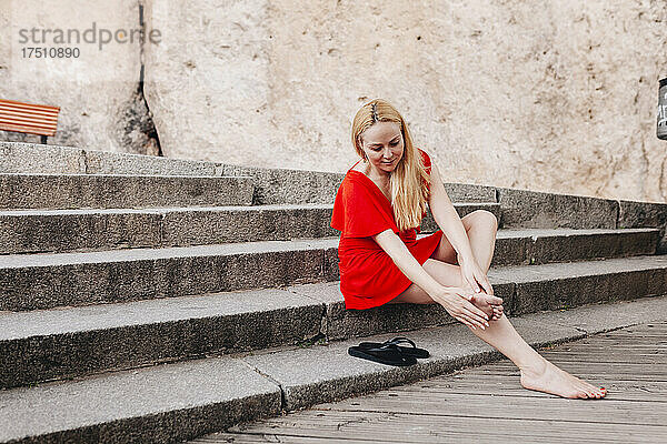 Frau in rotem Kleid sitzt auf Stufen und massiert ihren Fuß