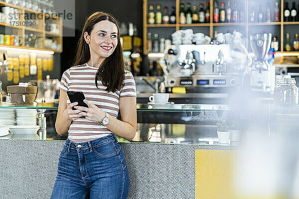 Nachdenkliche Frau hält Smartphone in der Hand  während sie im Café steht