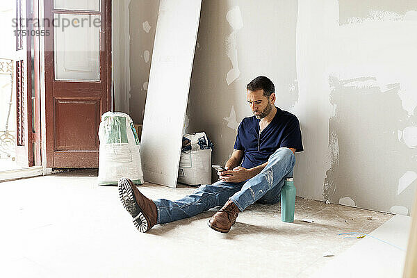 Arbeiter macht Pause in einem im Bau befindlichen Haus und nutzt dabei sein Mobiltelefon