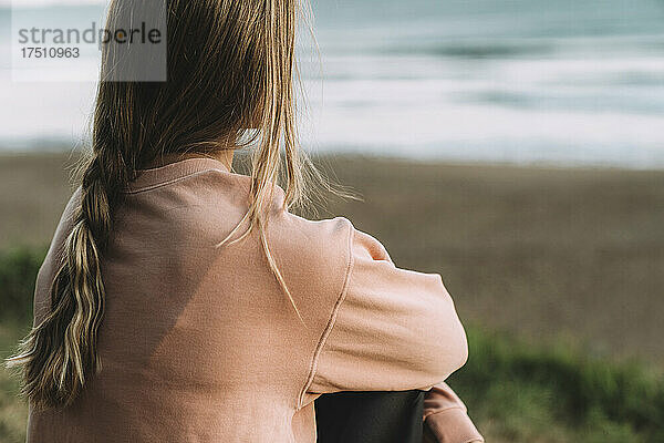 Nahaufnahme einer jungen Frau mit geflochtenem Haar  die bei Sonnenuntergang am Strand sitzt