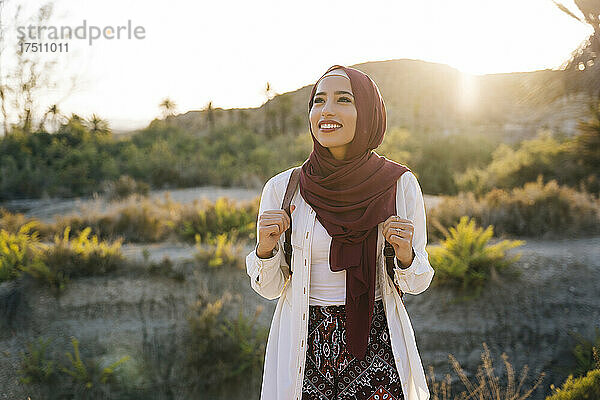 Lächelnde junge Touristin mit Hijab in der Wüstenlandschaft  die sich umschaut