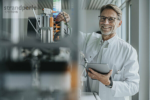 Lächelnder reifer Mann mit digitalem Tablet  der im Labor Maschinen erfindet