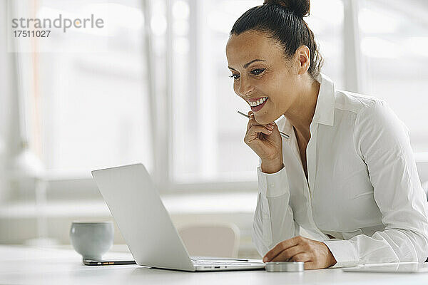 Lächelnde Geschäftsfrau benutzt Laptop auf dem Schreibtisch im Heimbüro