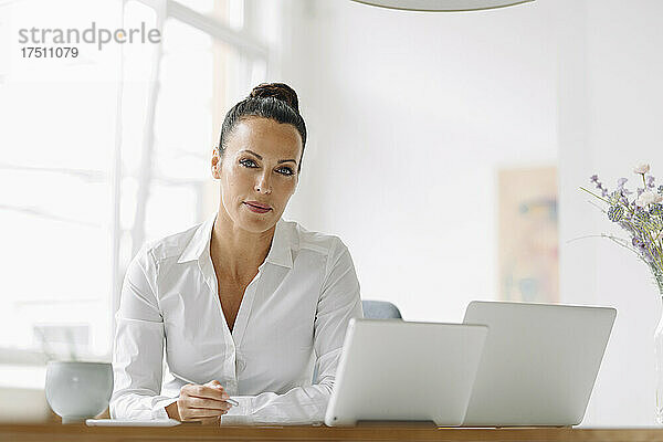 Selbstbewusste Geschäftsfrau mit Laptops auf dem Schreibtisch  die im Heimbüro arbeitet