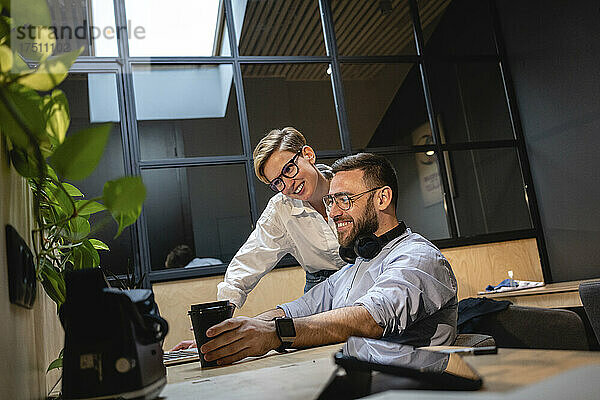 Lächelnde Unternehmer und Unternehmerinnen schauen auf den Laptop  während sie im Büro eine Strategie planen