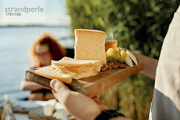 Mann serviert Käseplatte für Freunde an einem See
