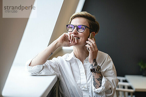 Lächelnde Geschäftsfrau  die mit dem Handy telefoniert  während sie durch das Fenster in der Bürokantine schaut