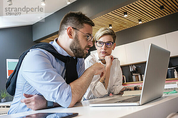 Selbstbewusste männliche und weibliche Fachkräfte planen Strategie  während sie im Büro am Laptop diskutieren