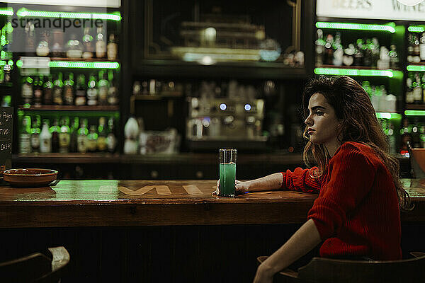 Nachdenkliche Frau mit Getränk an der Bartheke sitzt im Restaurant