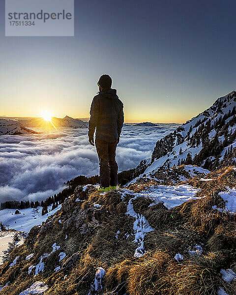 Mann bewundert den Sonnenaufgang über dem in Nebel gehüllten Bergtal