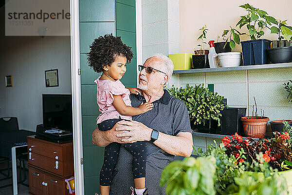 Großvater mit Sonnenbrille trägt Enkelin auf Balkon