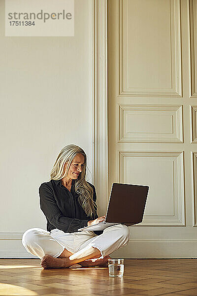 Lächelnde Frau benutzt Laptop  während sie zu Hause auf dem Boden sitzt