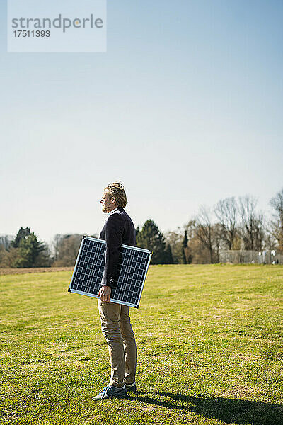Männlicher Unternehmer hält Solarpanel in der Hand  während er an einem sonnigen Tag in den Park blickt